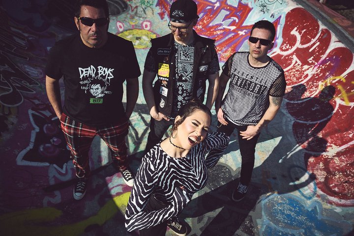 Punk-Band mit drei Männern und einer Frau in einem graffiti-bedeckten Skatepark.