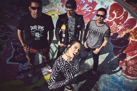 Punk-Band mit drei Männern und einer Frau in einem graffiti-bedeckten Skatepark.