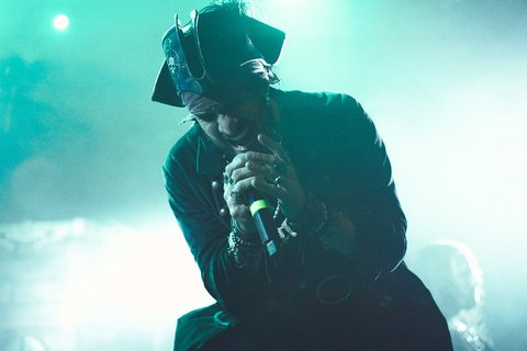 Ein Musiker in Piratenkostüm steht auf der Bühne und singt in ein Mikrofon. Stimmungsvolle Lichter und Rauch erzeugen eine lebhafte Atmosphäre. Der Musiker wirkt intensiv und leidenschaftlich während seiner Darbietung.