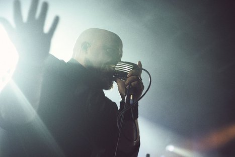 A singer passionately performs on stage, holding a vintage microphone. His hand is raised, conveying emotion as he engages with the audience. The scene is illuminated by dramatic lighting, creating a lively atmosphere.