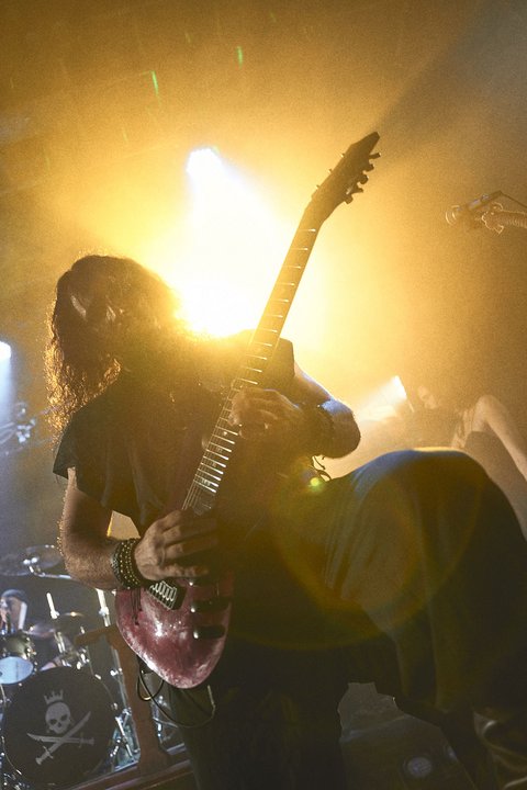 Ein Musiker spielt leidenschaftlich Gitarre auf der Bühne, umgeben von hellem Licht und einer energetischen Atmosphäre. Die Musik verkörpert Intensität und Emotion, während der Fokus auf dem Musiker und seinem Instrument liegt.