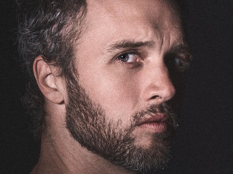 Ein Mann mit Bart und Tätowierungen schaut ernst in die Kamera.