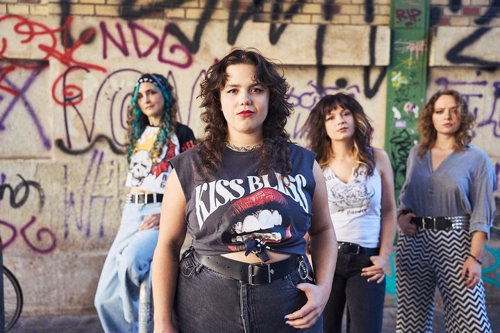 Vier junge Frauen im urbanen Stil posieren vor einer Graffitimauer.