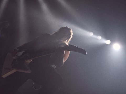 Ein Musiker spielt leidenschaftlich Gitarre auf der Bühne. Starke Lichteffekte und Nebel schaffen eine dynamische Atmosphäre. Die Silhouette des Musikers hebt sich dramatisch vor den Lichtern ab und vermittelt ein Gefühl von Energie und Intensität.