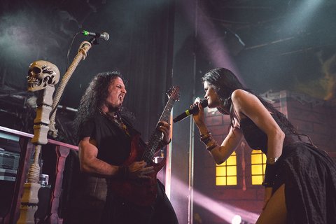 Zwei Musikerinnen auf der Bühne während eines Konzerts. Eine spielt Gitarre, die andere singt leidenschaftlich ins Mikrofon. Dramatische Beleuchtung sorgt für eine eindrucksvolle Atmosphäre.