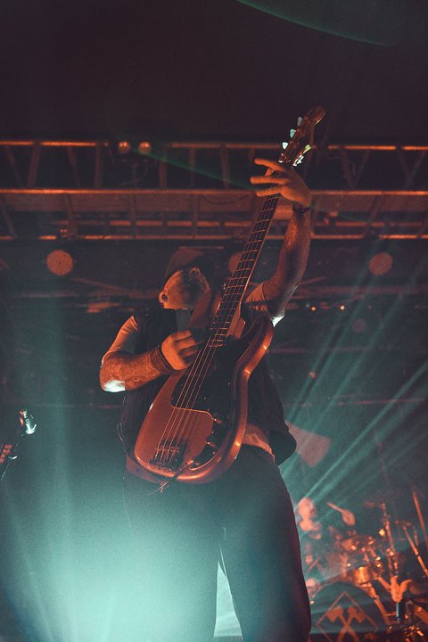 Ein Musiker spielt energetisch E-Gitarre auf einer Bühne, umgeben von bunten Lichtern. Die Szenerie vermittelt eine lebhafte Konzertatmosphäre.