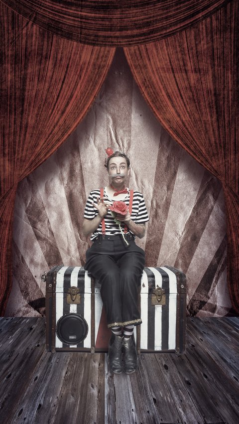 Eine Person in gestreifter Kleidung sitzt auf einem Koffer und hält ein Notizbuch. Sie hat Hasenohren auf und schaut nachdenklich. Der Hintergrund zeigt einen roten Vorhang und eine gestreifte Wand, die an ein Zirkuszelt erinnert.