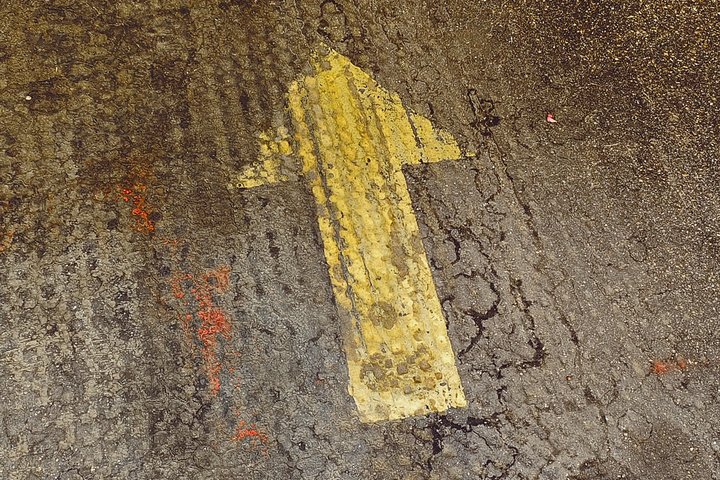 Gelbe Pfeilmarkierung auf einem rauen Boden, die nach oben zeigt. Sie weist den Weg oder signalisiert die Richtung.