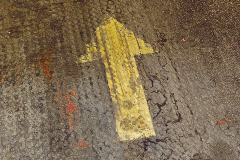 Gelbe Pfeilmarkierung auf einem rauen Boden, die nach oben zeigt. Sie weist den Weg oder signalisiert die Richtung.